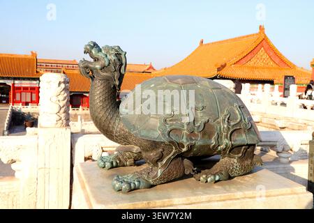This is a bronze statue of a bixi (dragon turtle) standing on a white marble plinth, its deep antique bronze surface mottled with green patina from ce Stock Photo