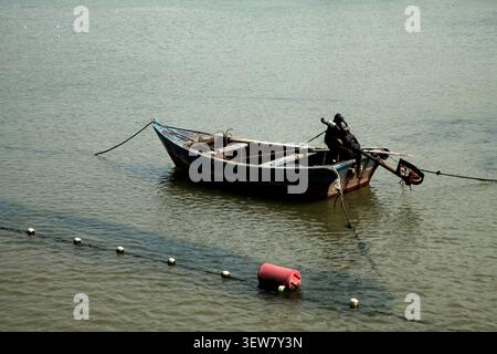 A weathered small fishing boat rests gently on the calm sea, its dark hull showing faded patches of blue paint and signs of long-term use. The black m Stock Photo