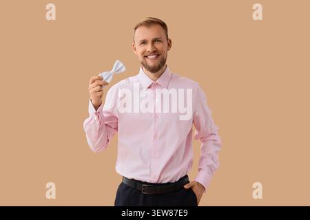 Smiling man holding white bow tie on beige background Stock Photo