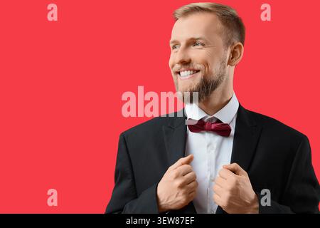 Smiling man in tuxedo adjusting jacket on red background Stock Photo