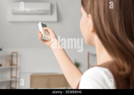 Woman using remote control to operate air conditioner Stock Photo