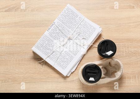 Stack of newspapers tied with string and two takeaway coffee cups on wooden table Stock Photo