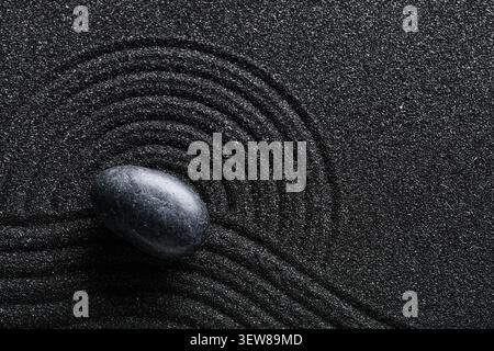 Black zen stone on black sand with concentric circles Stock Photo