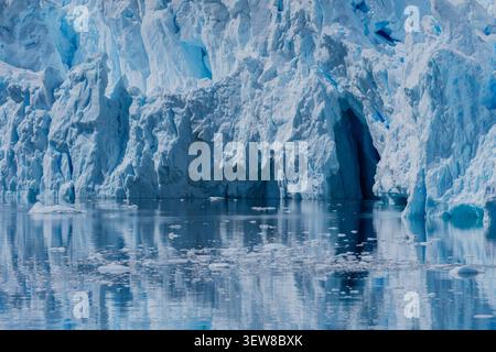 Close-up of a towering Antarctic glacier reflected in calm polar waters, revealing brilliant blue glacial ice and ice cave Stock Photo
