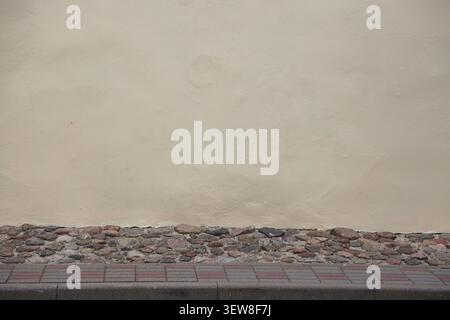 Full frame view of a smooth beige stucco wall texture above a decorative natural stone ground section. The composition features a modern minimalist co Stock Photo
