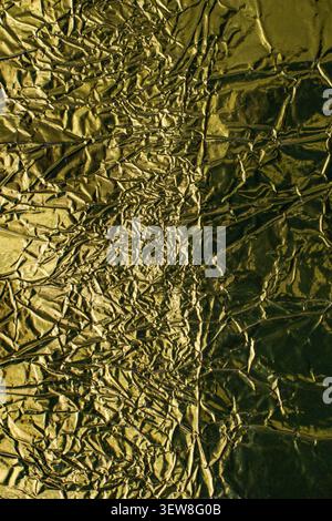Full frame background of creased and crumpled golden metallic foil with shiny reflective highlights. This abstract wrinkled tinfoil texture with deep Stock Photo
