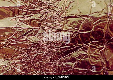 Full frame background of creased and crumpled bronze or rose gold metallic foil with shiny reflective highlights. This abstract wrinkled tinfoil textu Stock Photo