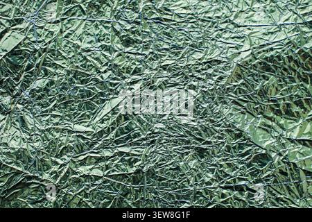 Full frame background of creased and crumpled light green or mint aluminum foil with shiny reflective highlights. This abstract wrinkled metallic text Stock Photo
