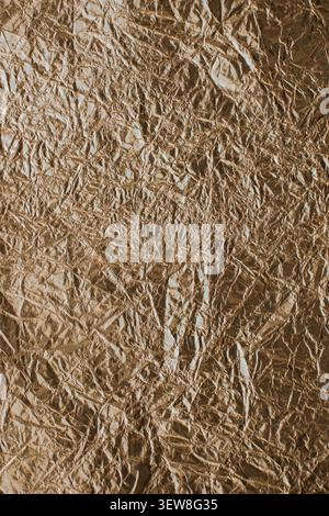 Full frame background of heavily creased and crumpled brown or chocolate metallic foil with shiny reflective highlights. This abstract wrinkled tinfoi Stock Photo