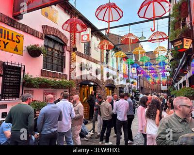 Crowded alleyway at Duke of York pub in Cathedral Quarter, Belfast, Northern Ireland, featuring overhead colorful hanging umbrella canopy. Stock Photo