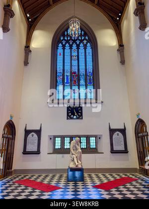 The Great Hall interior, Queen's University, Belfast, Northern Ireland. Featuring a stained glass window, arched doorways, and a stone statue. Stock Photo