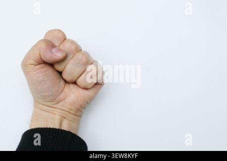 Detailed closeup of a man's clenched fist held up against a clean white surface with copy space. This powerful gesture represents strength, power, pro Stock Photo