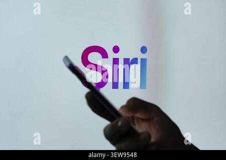 Screen displaying 'Siri' with a hand holding a smartphone in the foreground Stock Photo