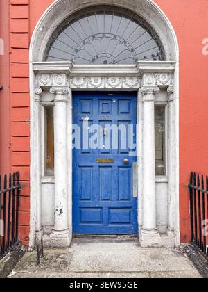 A bright blue front door of a Georgian house in Dublin, Ireland, featuring a semi-circular fanlight, white columns, and ornate detailing. Stock Photo