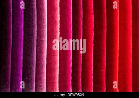 Close up of folded velvet fabric samples arranged in vertical stripes showing a color gradient from dark purple to bright red Stock Photo