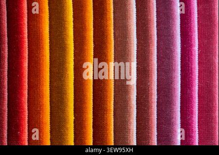 Macro close up of folded velvet fabric samples arranged in vertical stripes showing a warm color gradient from red and orange to brown and pink Stock Photo