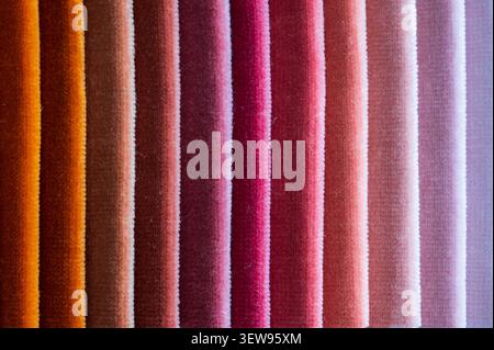 Macro close up of folded velvet fabric samples arranged in vertical stripes showing a warm color gradient from deep orange to light pink Stock Photo