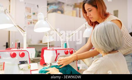 Young woman teaching older woman sewing machine operation Stock Photo