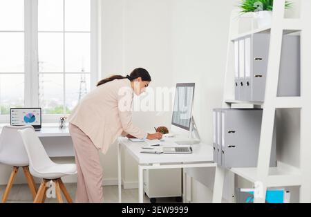 Female auditor analyzing paperwork at desktop computer in bright modern office Stock Photo