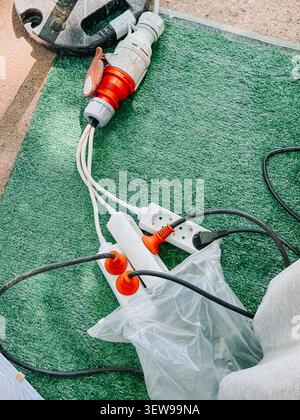 Industrial electrical extension cords, power strips, and heavy-duty connectors arranged on artificial grass at an outdoor worksite. Practical image fo Stock Photo