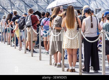 People stand in line alone, as a couple, in a group, with family or friends at the entrance of a tourist site, on a sunny summer day. Stock Photo