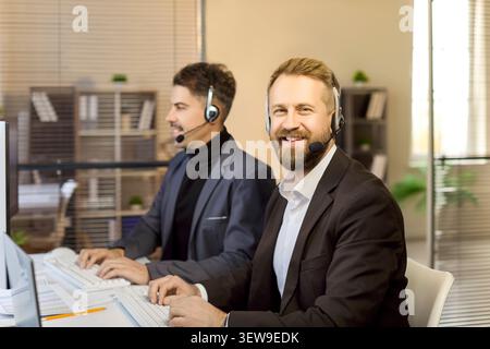 Happy customer service representatives using headsets at computers in bright office Stock Photo