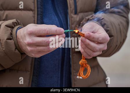 Close up of man hand lighting up a firecrackers with wick. Man holding a burning petard in his hand. Stock Photo