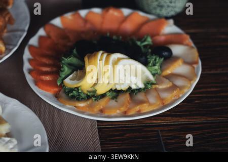 Freshly arranged seafood platter gleams invitingly. Sliced lemon, greens, and citrus adorn the dish. Platter rests on dark wood table, softly lit Stock Photo