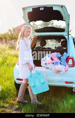 Stylish woman posing outdoors with a picnic accessory and floral arrangement, creating a cozy road trip and weekend escape concept Stock Photo