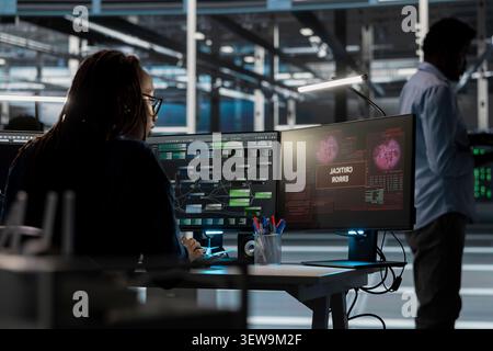 Concerned female IT worker reviews warning messages in a data center while troubleshooting errors affecting equipment performance. Stock Photo
