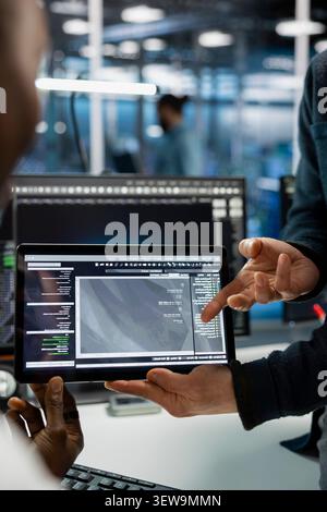 Data center programmers use a digital tablet in a data center to deploy software updates, configure hardware, and support reliable operations. Stock Photo