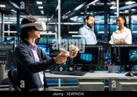 Data center programmer uses a VR headset to analyze datasets and manage AI database workflows in a server room. Stock Photo