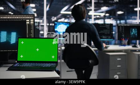 Software developer uses a green screen laptop to manage AI systems, machine learning workflows and server performance. Stock Photo