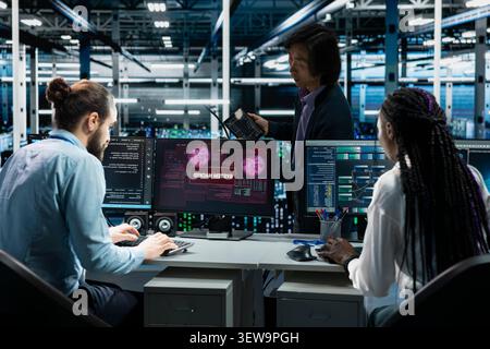 Engineering team reviews a security breach alert for a zero-day vulnerability inside a high-tech server room. Stock Photo