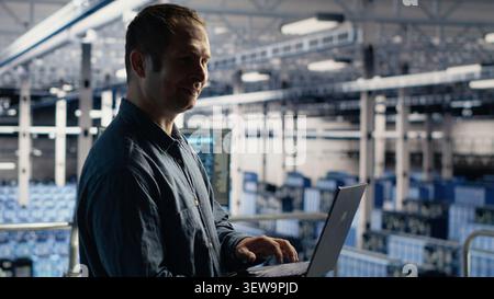 Data center technician monitors AI systems and machine learning workloads on a laptop inside a high-tech server facility. Stock Photo