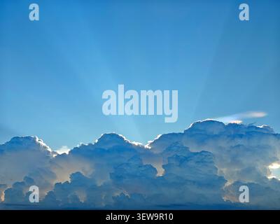 The image shows a beautiful blue sky with numerous white clouds scattered across it The sun is shining brightly from the top right corner creating a s Stock Photo