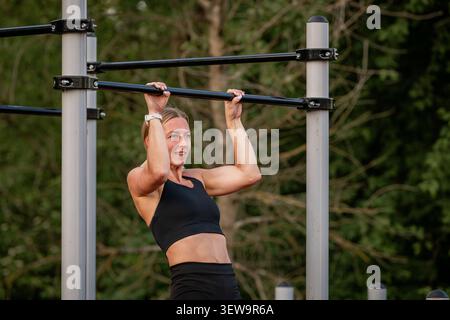 Athletic woman doing pull ups at an outdoor gym Stock Photo