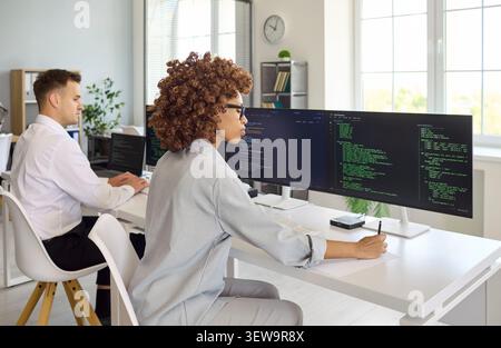 Female developer coding at multi monitor setup in contemporary collaborative office Stock Photo