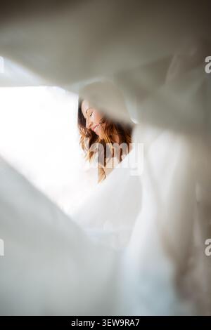 Happy woman smiling from behind white fabric Stock Photo