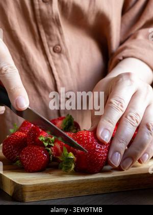 Woman slicing fresh strawberries on wooden cutting board in home kitchen. Healthy dessert preparation, ingredient processing, homemade food and season Stock Photo