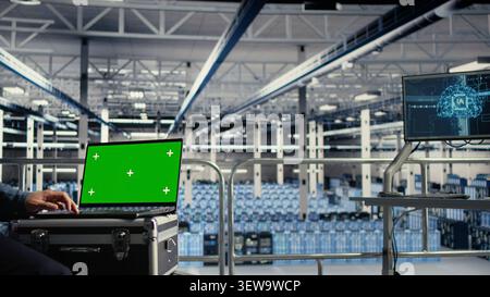 Data center worker uses a green screen laptop in a server room for AI workflow and screen replacement. Stock Photo