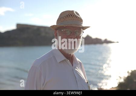 Elderly man in a straw hat smiles by the sea Stock Photo