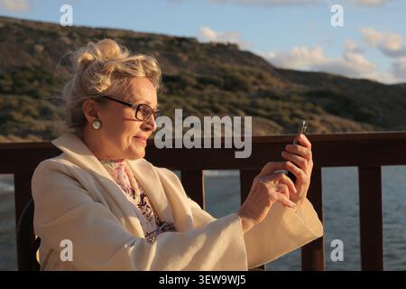 Elegant senior woman using a smartphone by the sea Stock Photo