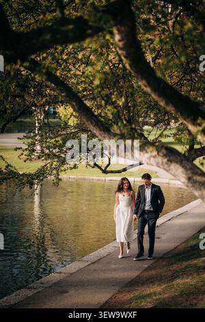 Elegant couple walks hand in hand by a park pond Stock Photo