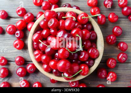 Ripe red cherries in a wooden bowl with scattered berries around on the table. Rustic style. Berries create an atmosphere of summer mood. Farm to tabl Stock Photo