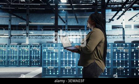 Data center engineer uses a laptop in a server room to upgrade server rigs and increase workload capacity. Stock Photo