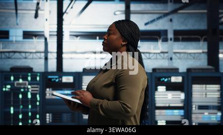 Data center technician monitors data center metrics on a digital device to improve equipment performance. Stock Photo