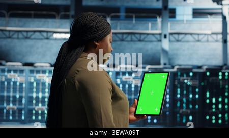 Data center worker uses a green screen tablet in a server room for AI workflow and screen replacement. Stock Photo