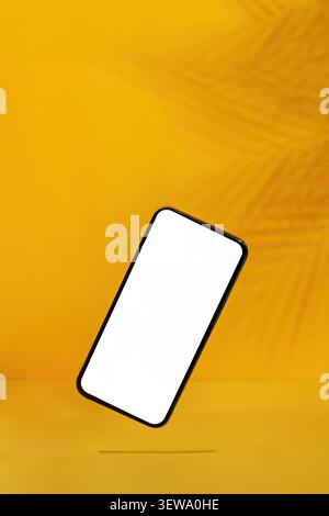 Floating smartphone mockup with blank screen on vibrant yellow background with shadow Stock Photo