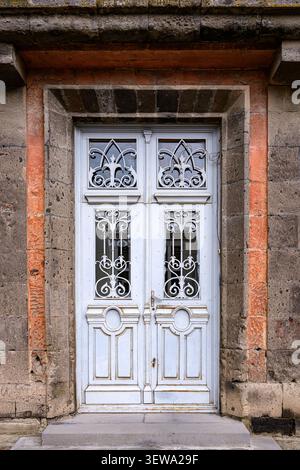 Old weathered double door with ornate wrought ironwork. Door set in stone frame with brick accents. Light blue paint peeling on wooden panels. Classic Stock Photo